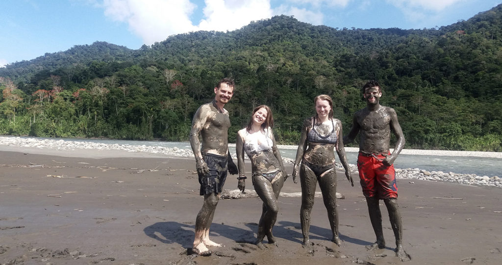 Travelers covered in river clay on a beach during the clay therapy