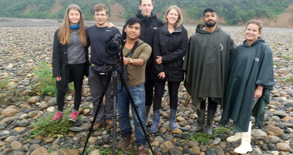 Group of travelers with their guide and a spotting scope on a river beach
