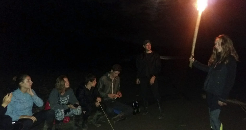 Viajeros alrededor de una antorcha en la orilla del río por la noche