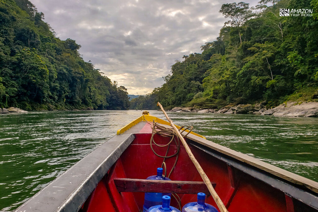 Proa de un bote de madera en un río entre colinas con bosque