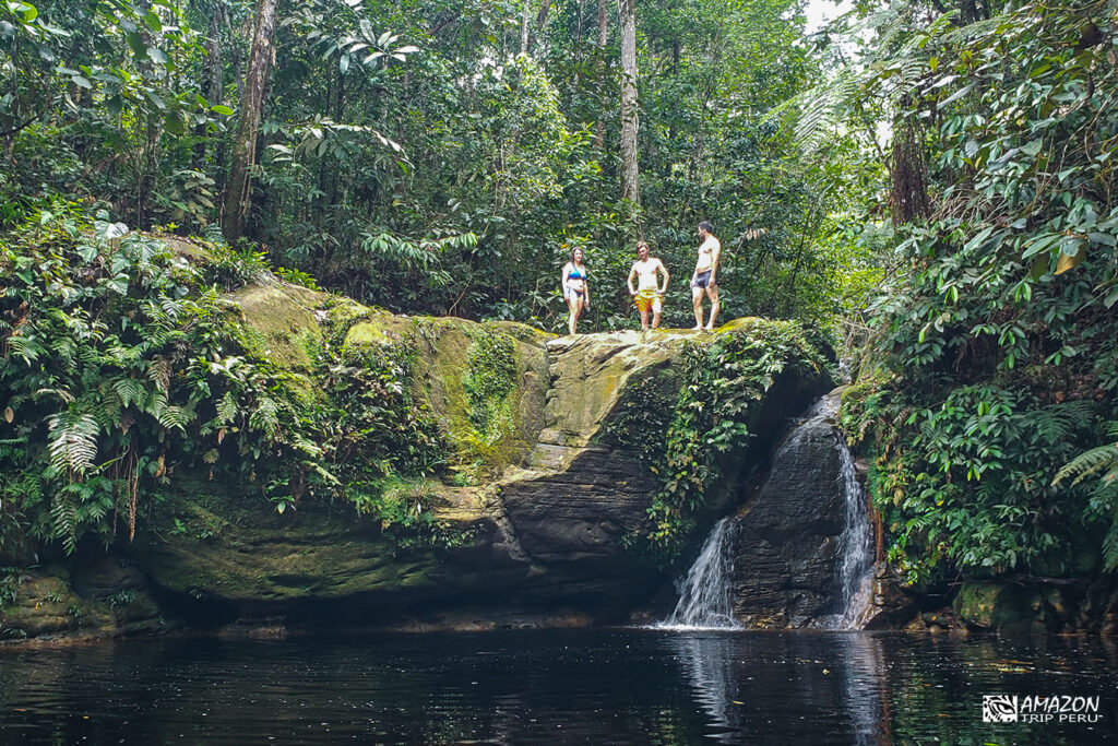 Viajeros sobre una roca junto a la poza de una cascada en el bosque